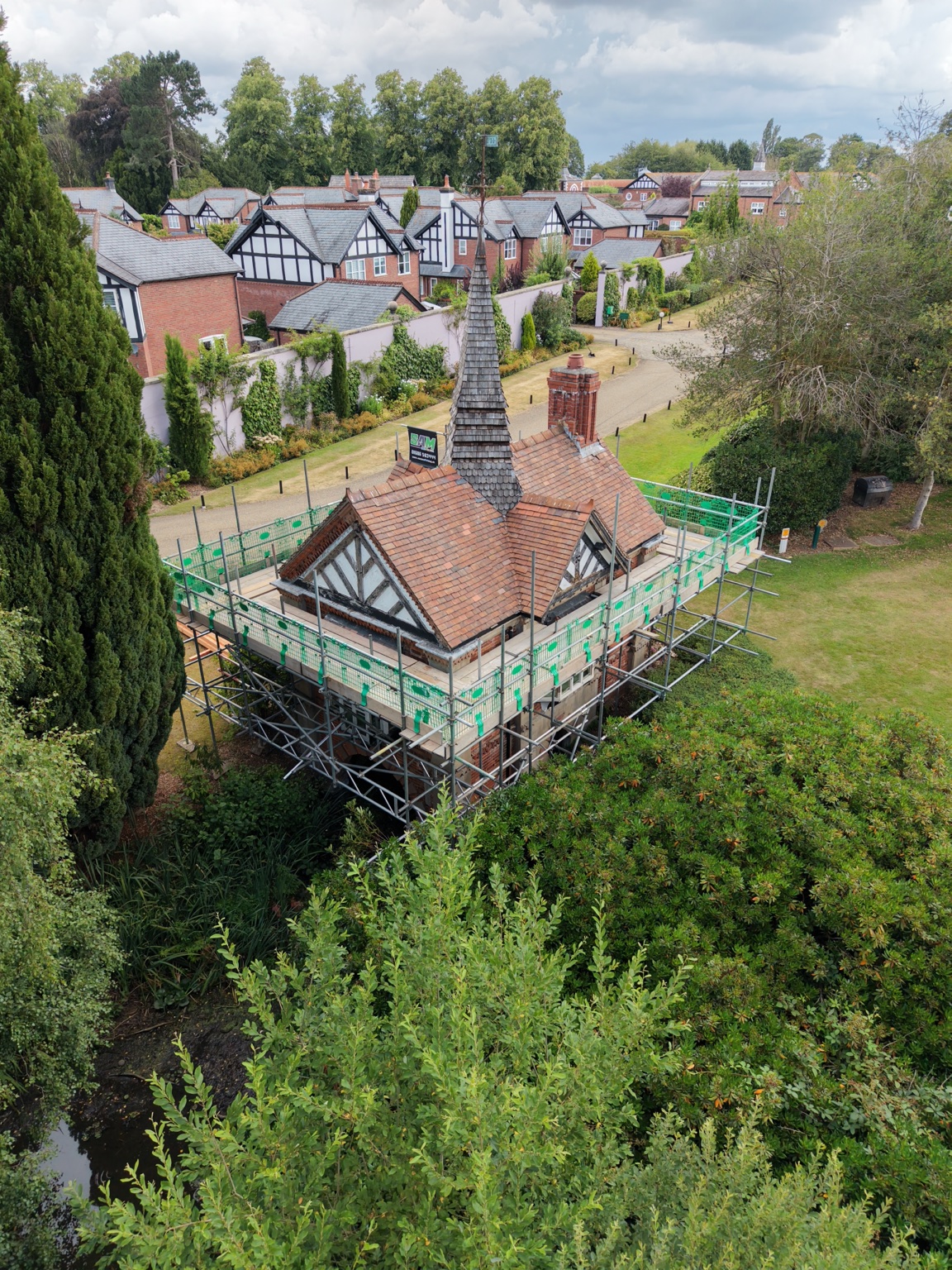 Drone view of the Victorian boathouse at Bostock Hall, with scaffold around its timbered gables and tiled roof